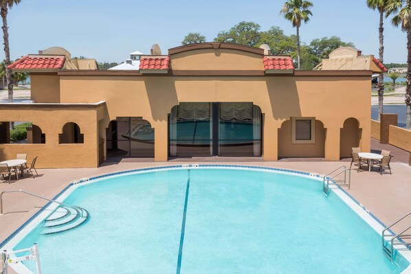 A pool area with a clear blue pool, a covered seating area, and a building with a red-tiled roof. - Days Inn by Wyndham St Augustine/Historic Downtown (St. Augustine)