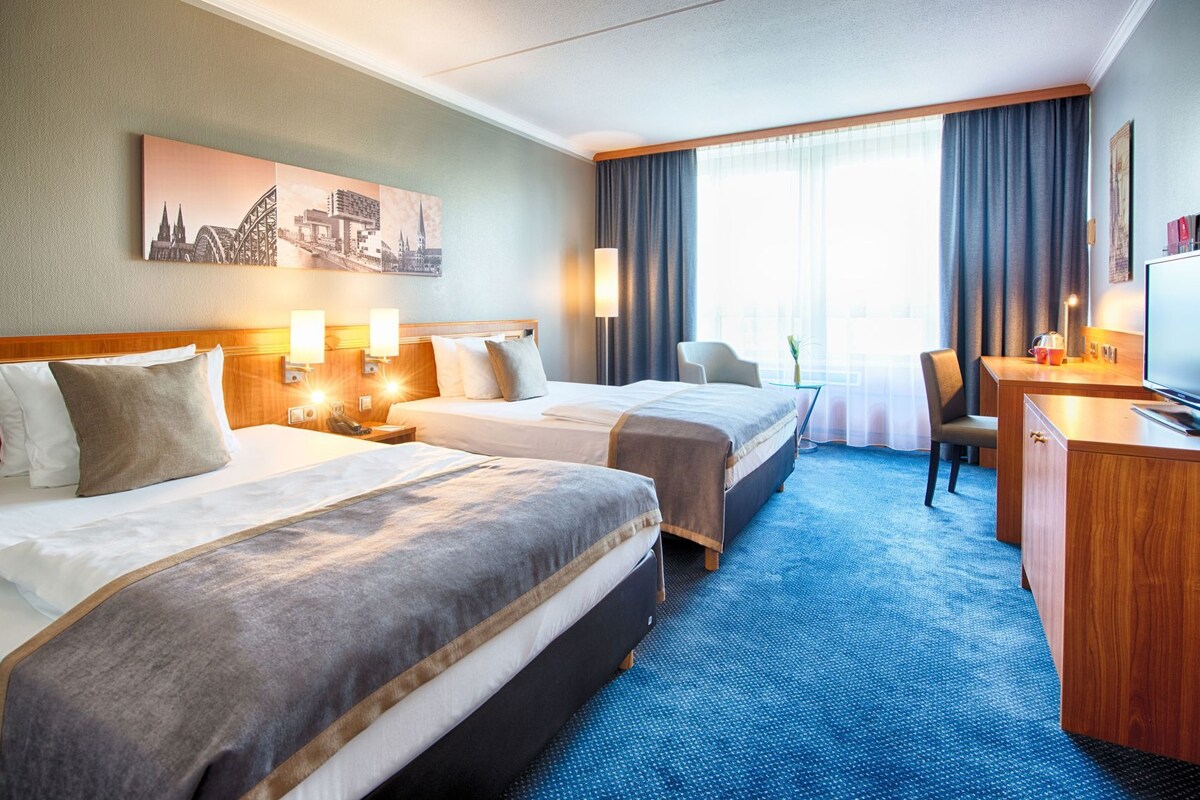 A hotel room with two beds, a desk, a chair, a television, and a window with curtains.