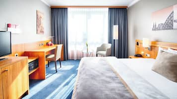 A hotel room with a large bed, a desk, a chair, a TV, and a window with curtains.