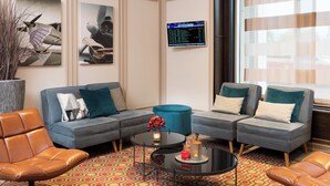 Una sala de estar moderna con un sofá seccional gris, dos sillones, una mesita de centro y un ventanal con cortinas traslúcidas.
