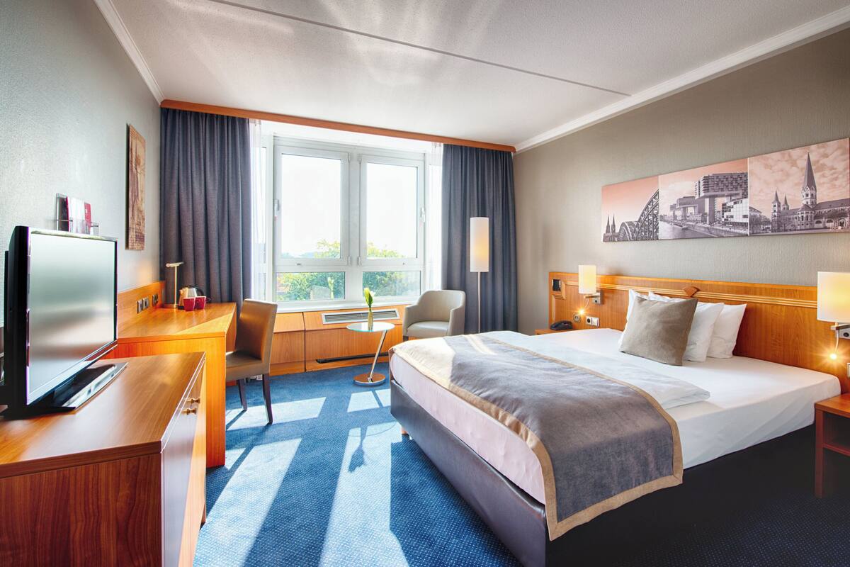 Une chambre d’hôtel avec un grand lit, un bureau avec un ordinateur, une chaise et une fenêtre avec des rideaux.