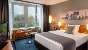 Una habitación de hotel con una cama grande, un escritorio con silla, un televisor y una ventana con cortinas.