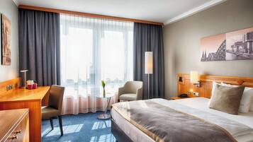 Ein Hotelzimmer mit einem großen Bett, einem Schreibtisch mit Stuhl, einem kleinen Tisch mit Vase und einem Nachttisch mit Lampe.