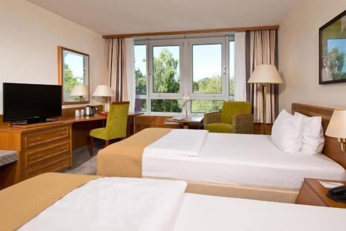 Une chambre d’hôtel avec deux lits, un bureau, une télévision et de grandes fenêtres.