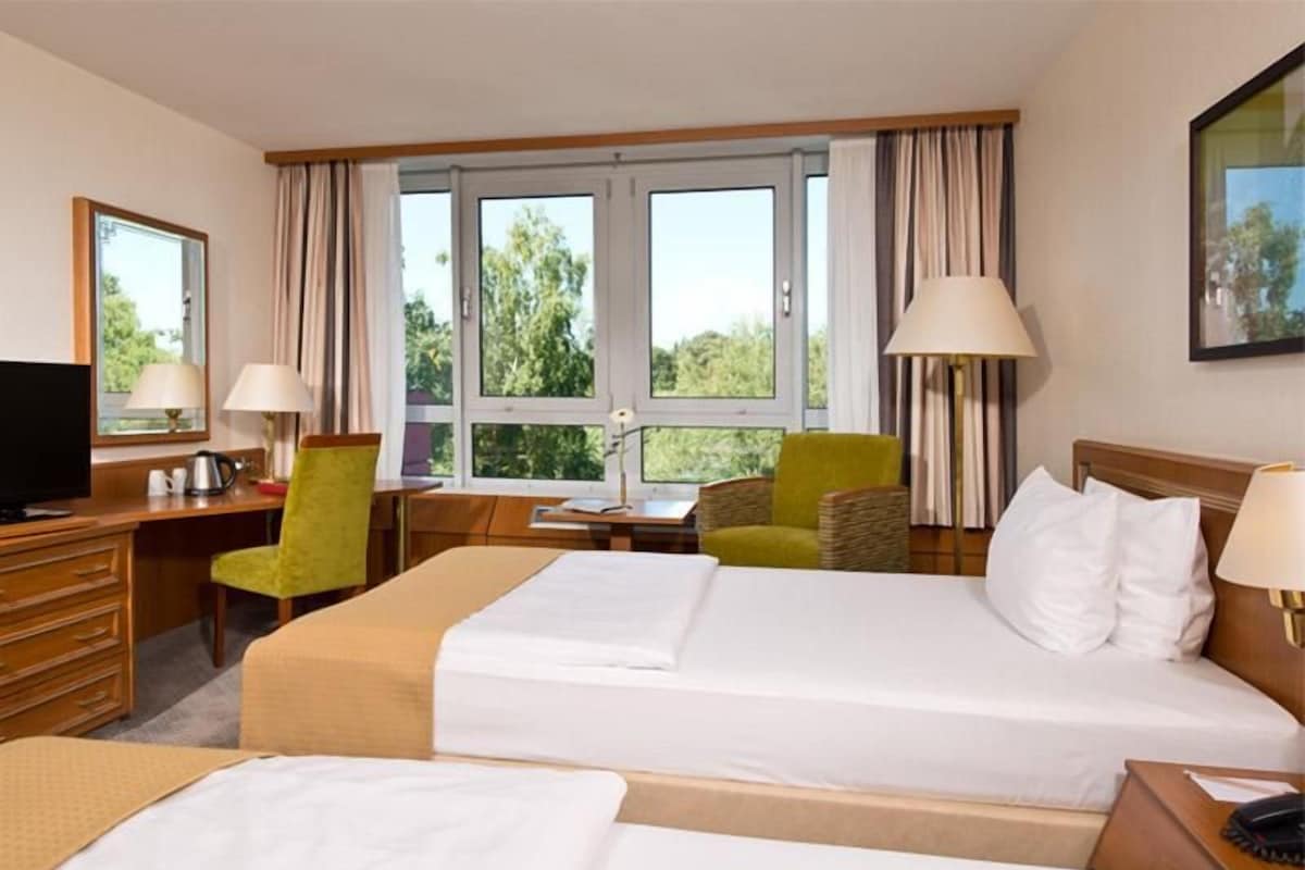 A hotel room with two beds, a desk, a chair, and a television.