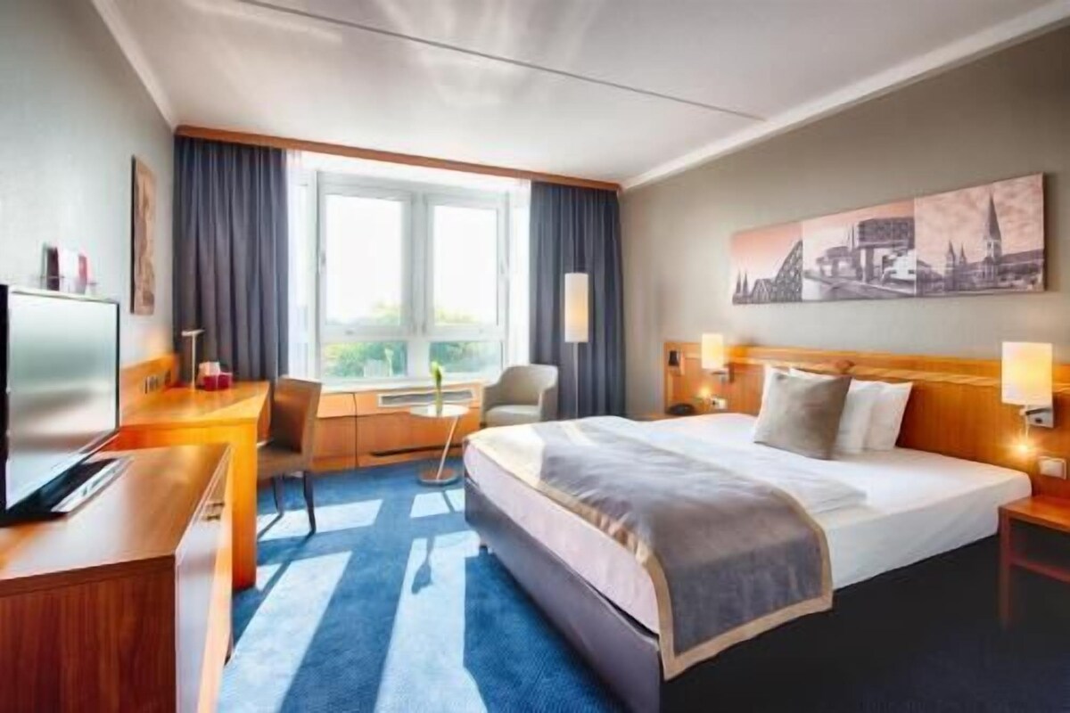 Habitación de hotel con cama, escritorio, silla y un ventanal grande.