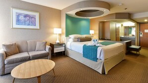 A hotel room with a bed, a sofa, a small table, a nightstand, a lamp, a mirror, and a framed picture on the wall. - Howard Johnson Plaza by Wyndham by the Falls Niagara Falls (Niagara Falls)