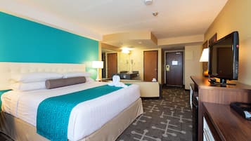 A hotel room with a large bed, a desk, a television, and a bathroom with a mirror and a shower.