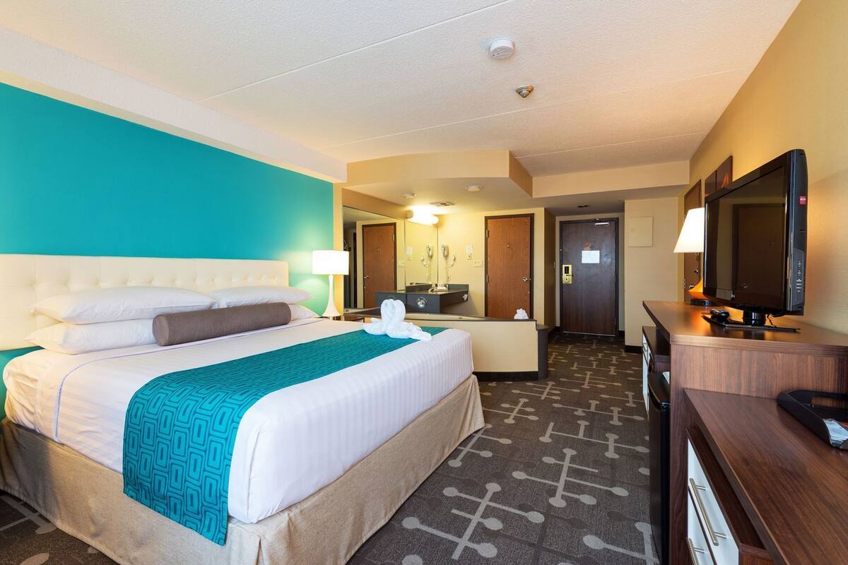 Une chambre d’hôtel avec un lit, un bureau, une télévision et une salle de bain que l’on aperçoit à l’arrière-plan.