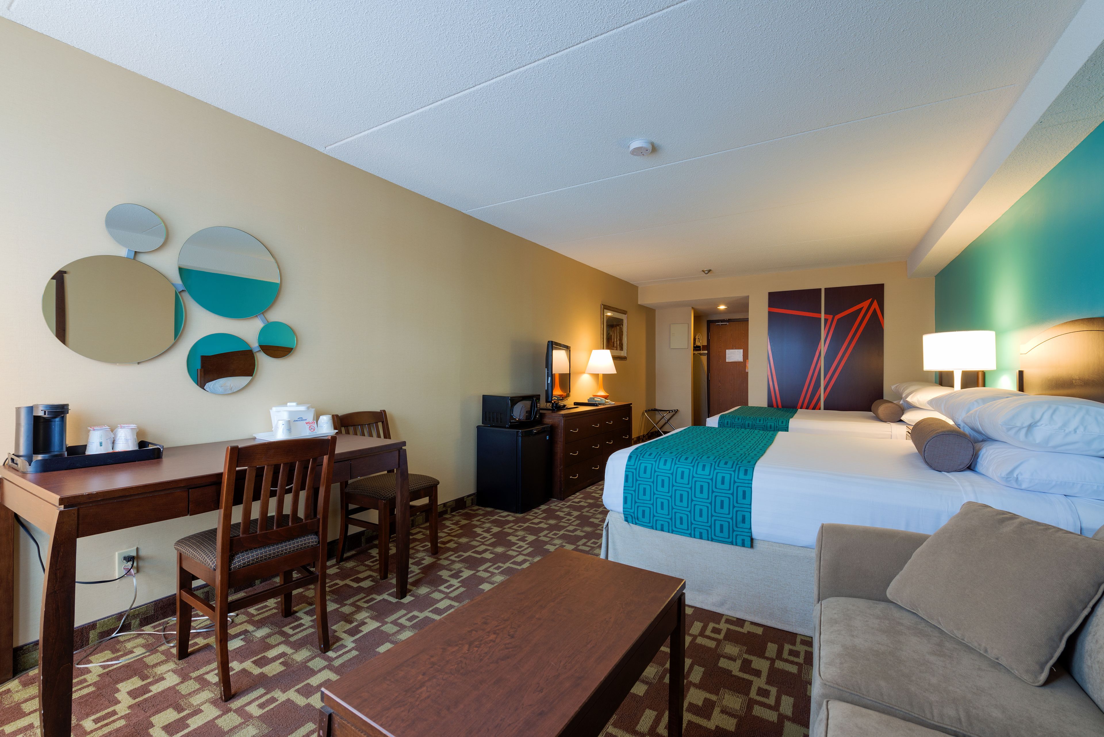 A hotel room with a bed, desk, chair, and a small table.
