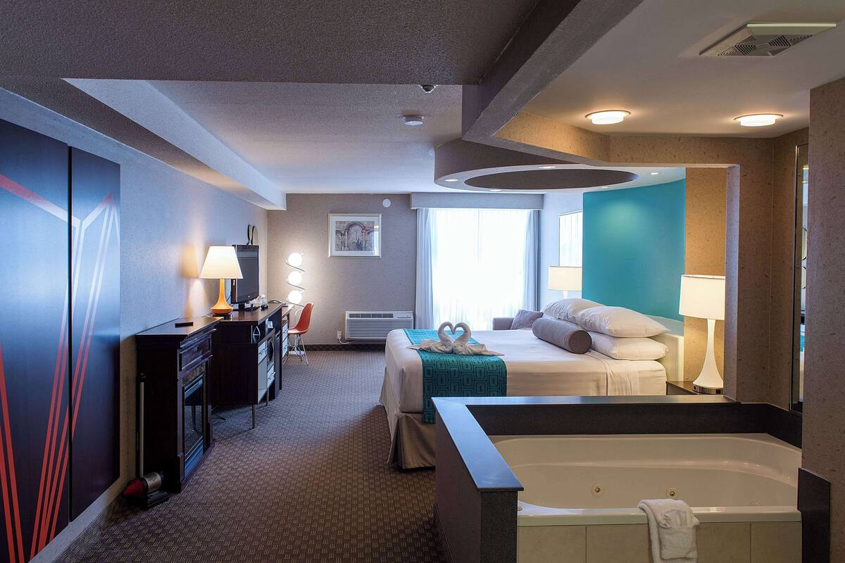 Une chambre d’hôtel avec un lit, un bureau doté d’une lampe, une grande fenêtre et une baignoire.