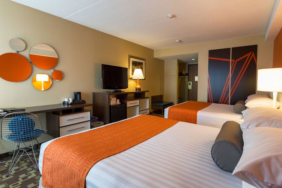 Une chambre d’hôtel avec deux lits, un bureau avec une chaise, une télévision et un miroir.