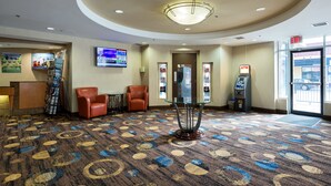 A lobby with a patterned carpet, a reception desk, a TV screen, a chair, an ATM, and an exit sign. - Howard Johnson Plaza by Wyndham by the Falls Niagara Falls (Niagara Falls)