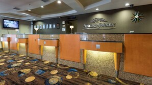A hotel reception area with a Howard Johnson sign, multiple reception counters, framed certificates, and a television on the wall. - Howard Johnson Plaza by Wyndham by the Falls Niagara Falls (Niagara Falls)