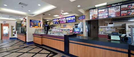 L’intérieur d’un restaurant de pizzas, avec un comptoir, des panneaux affichant le menu et un sol carrelé.