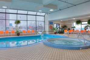An indoor swimming pool with orange chairs and potted plants.