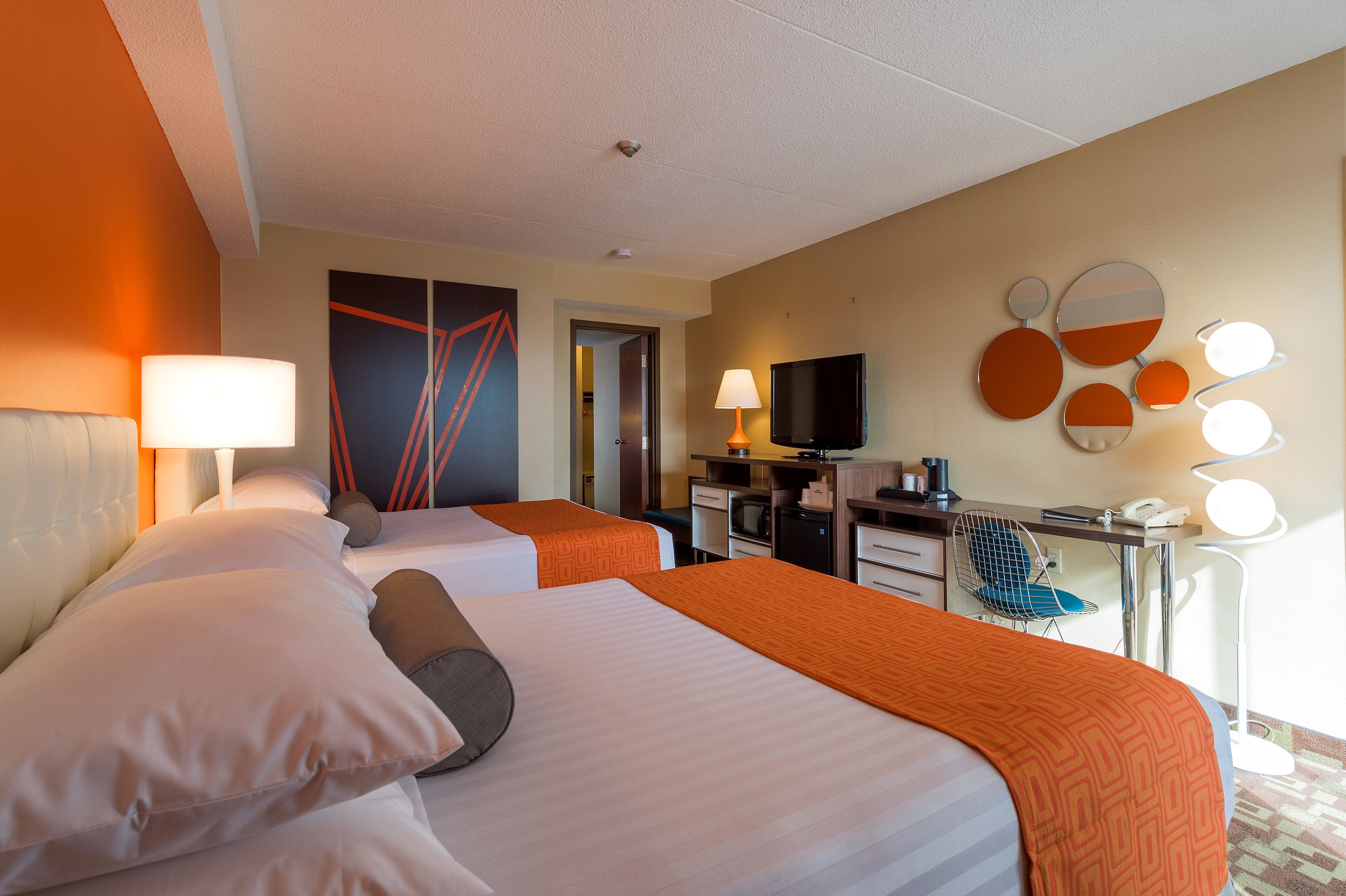 A hotel room with two beds, a desk with a computer, a TV, and a seating area with a chair.