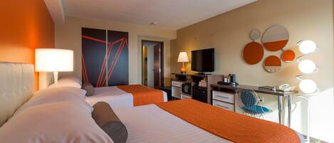 A hotel room with two beds, a desk with a computer, a TV, and a seating area with a chair.