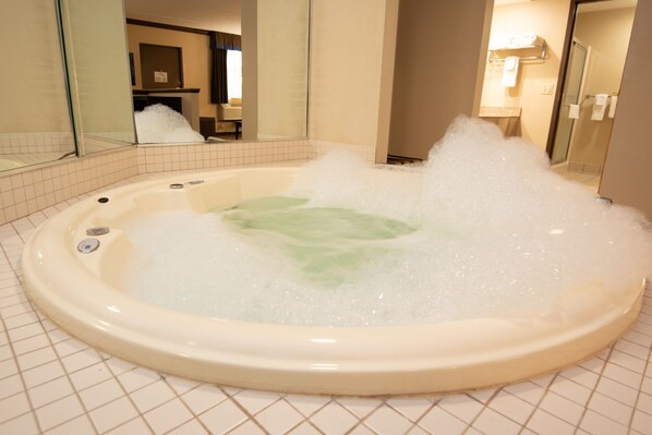 A hot tub filled with bubbles in a bathroom with tiled flooring and a mirror reflecting the room.