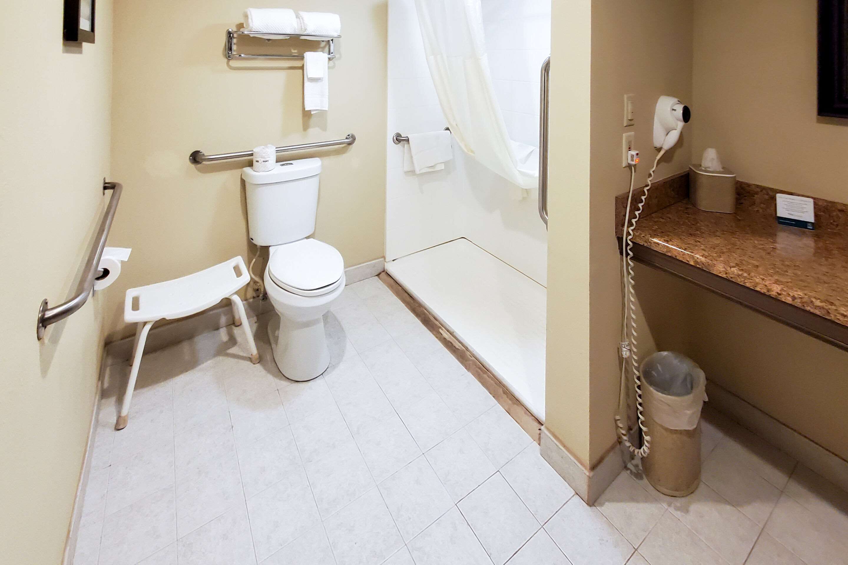 Een badkamer met toilet, greep, douchegordijn en prullenbak.