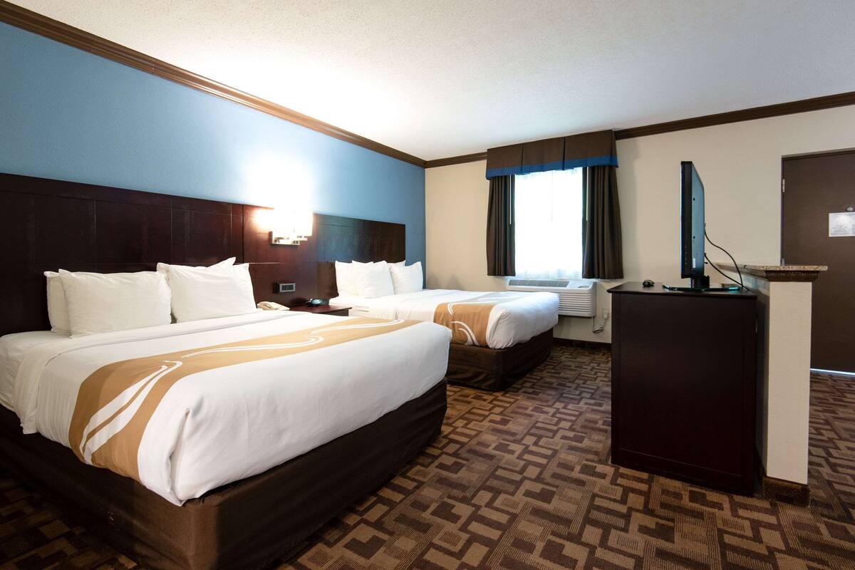 A hotel room with two beds, a desk, and a television.