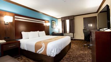 A hotel room with a large bed, a desk with a computer, a chair, a desk lamp, and a television.