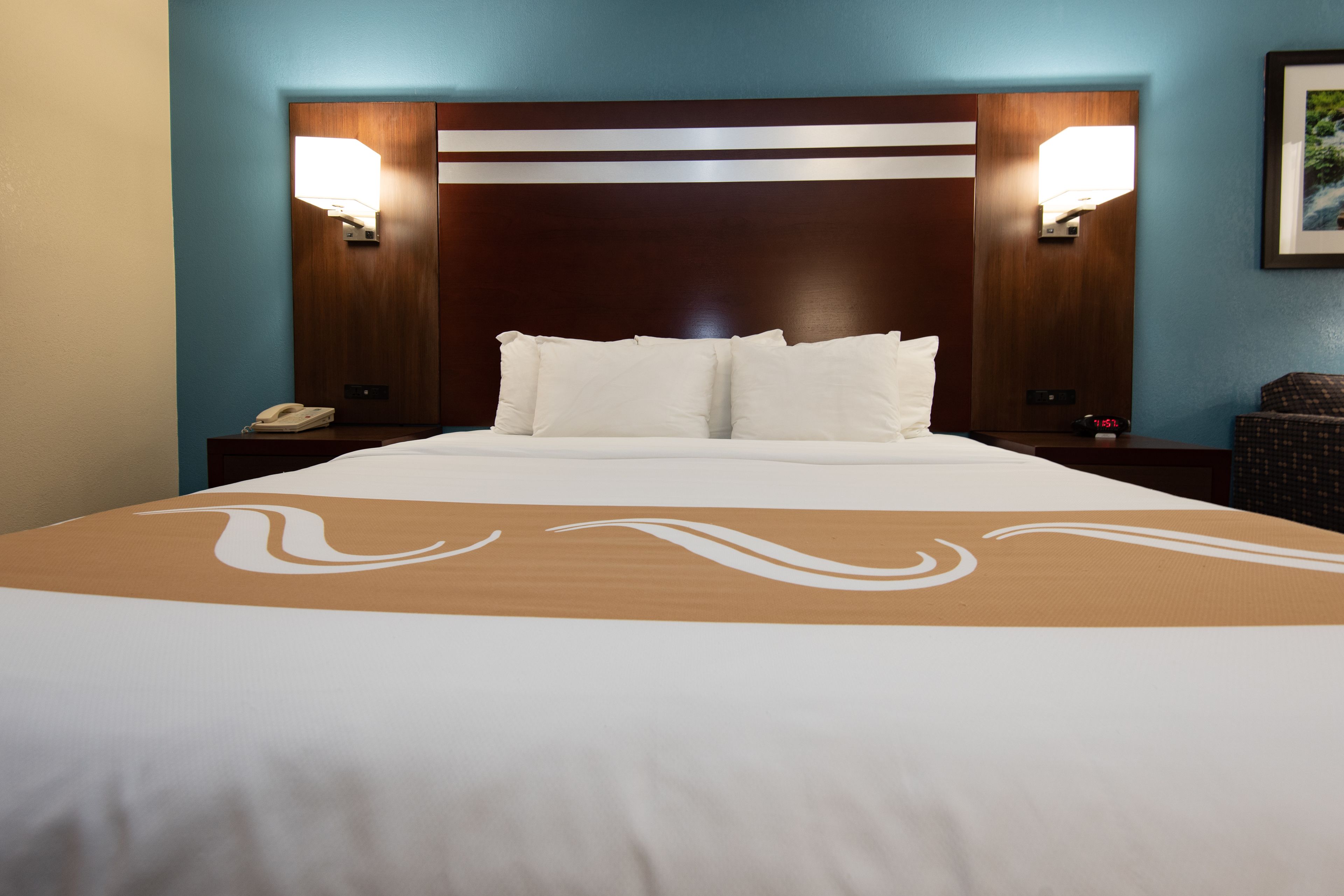 Quarto de hotel com uma cama grande, duas luminárias de cabeceira, uma mesa de cabeceira com telefone e cabeceira com luminária.