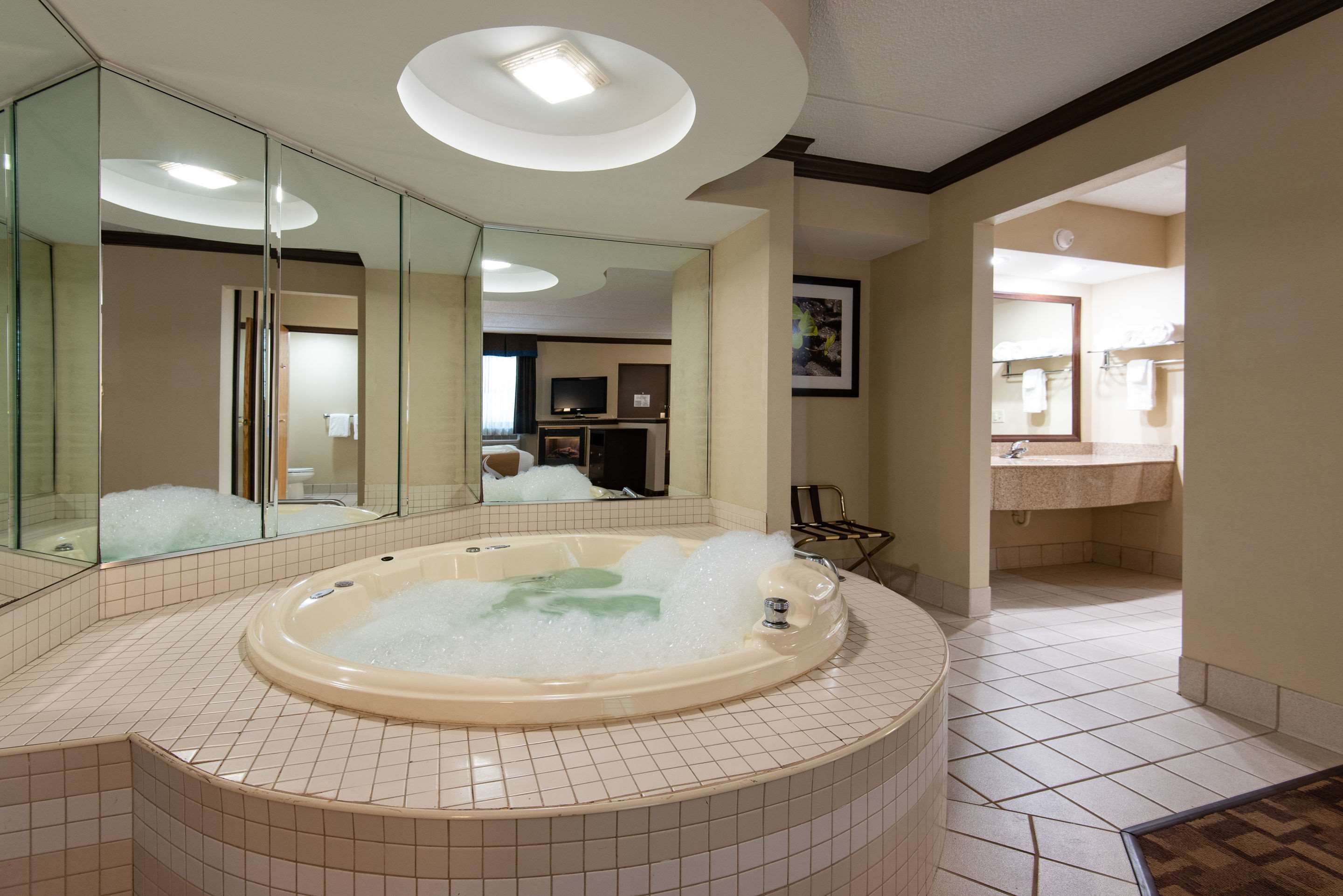 Une salle de bain moderne avec une grande baignoire remplie de mousse, un miroir et un espace douche séparé.