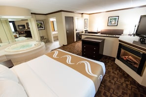 Habitación de hotel con una cama grande, una zona de estar con chimenea, una kitchenette y un baño con bañera.