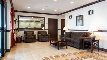 A spacious lobby with a reception desk, two armchairs, a sofa, and a patterned rug.
