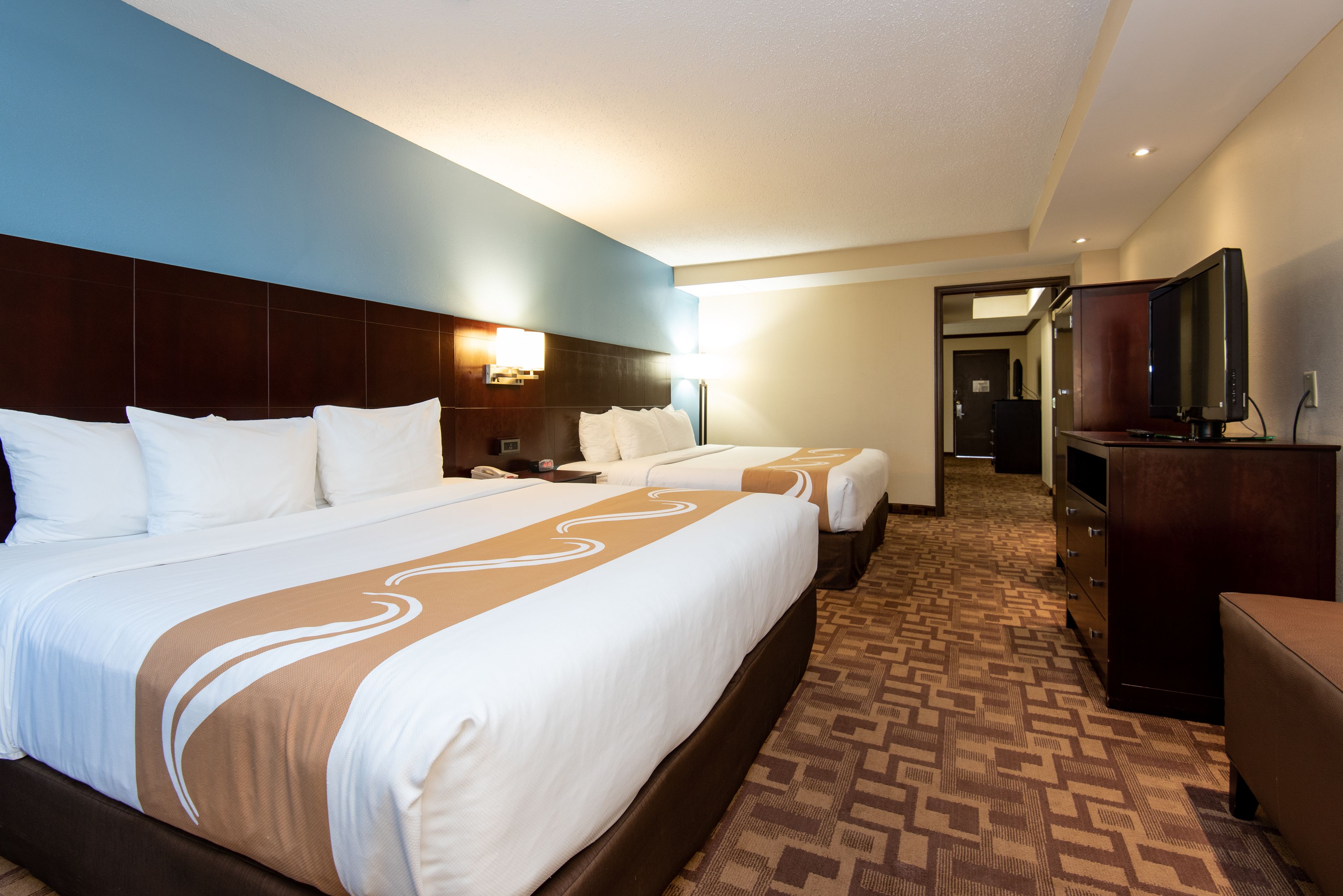 A hotel room with two beds, a desk, a dresser, and a television.