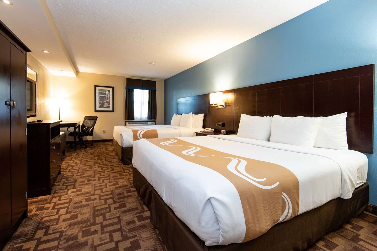 A hotel room with two beds, a desk, a chair, and a television.