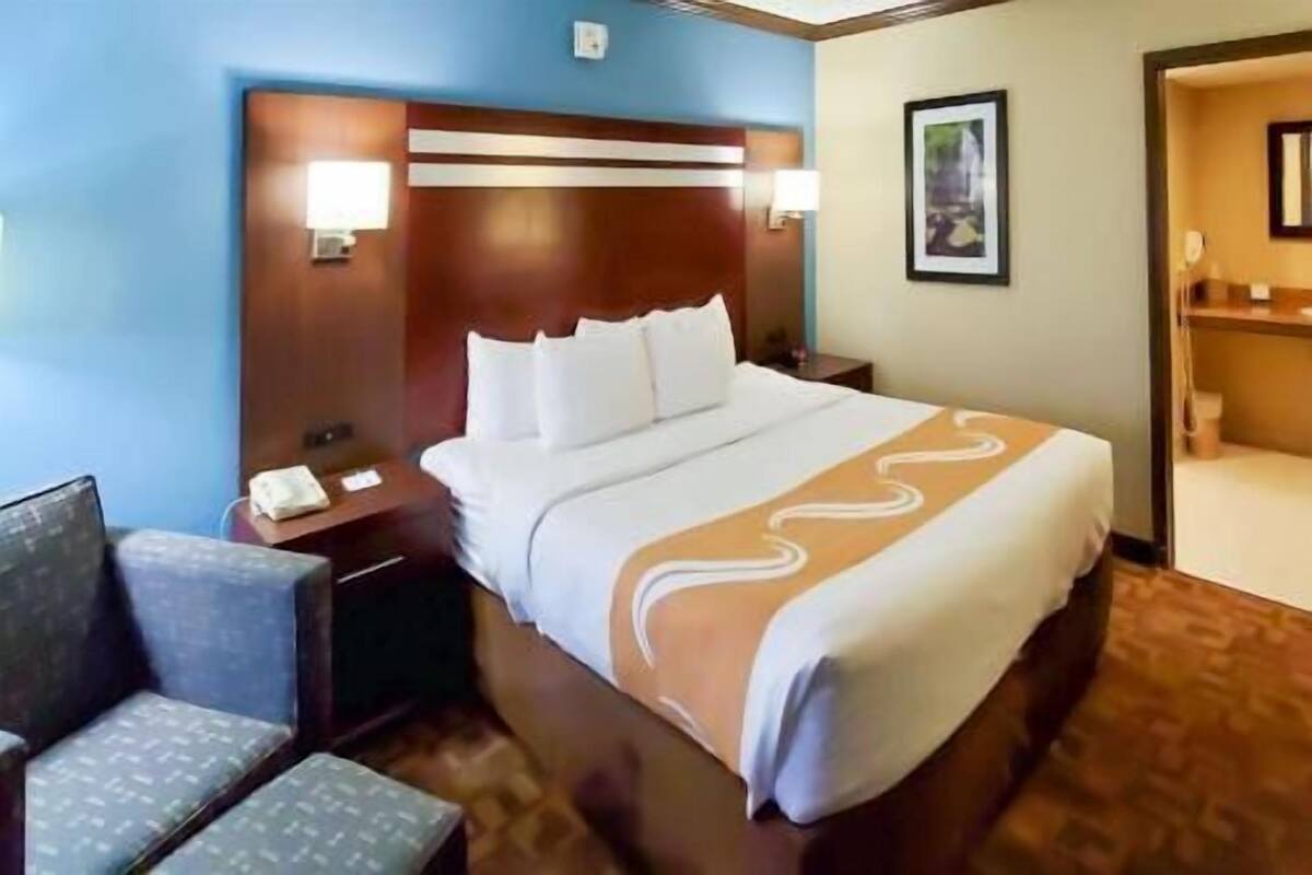 A hotel room with a large bed, a nightstand with a phone, a chair, and a picture on the wall.