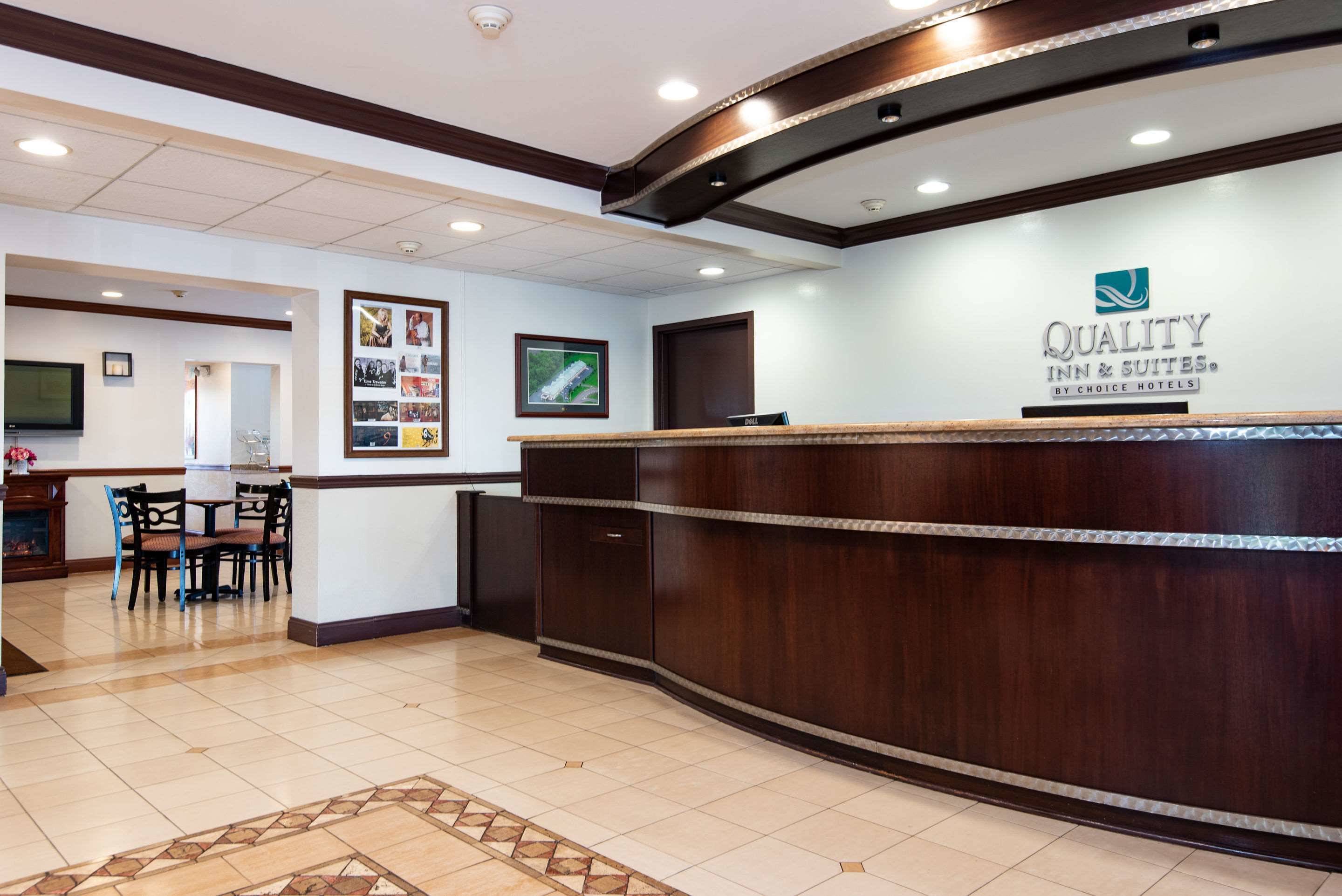 A hotel reception area with a wooden reception desk, a television mounted on the wall, and a framed photo collage.