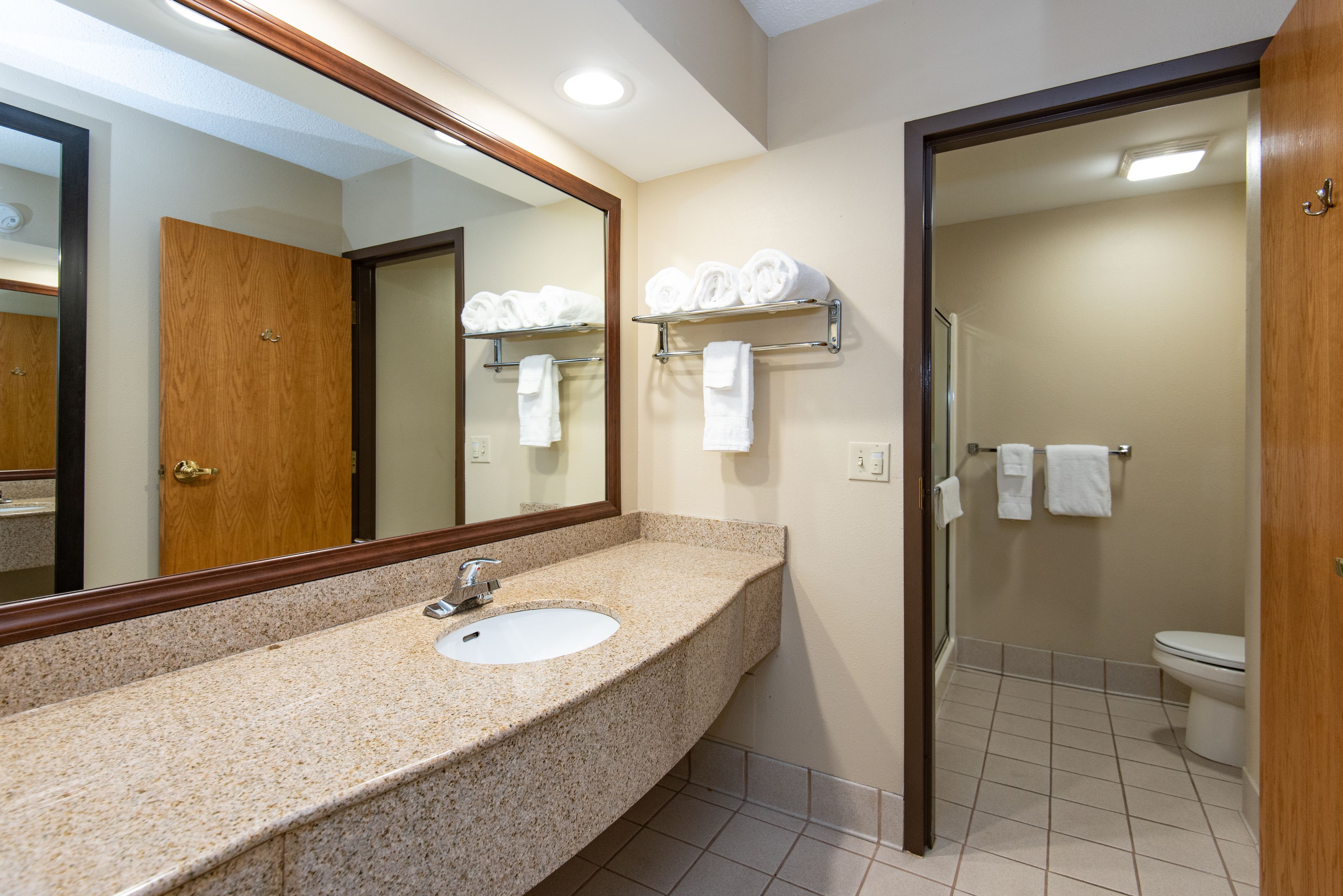 Une salle de bain avec un lavabo doté d’un plan de travail en granit, un grand miroir et un porte-serviettes.