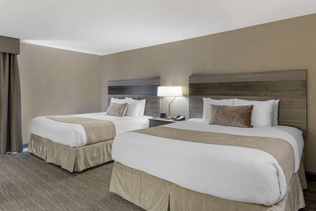 A hotel room with two beds, a nightstand, a lamp, and a large window with curtains.