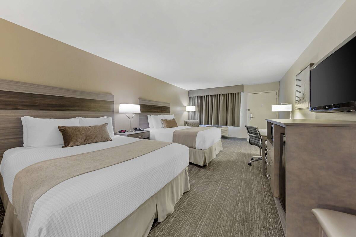 A hotel room with two beds, a desk, a TV, and a chair.