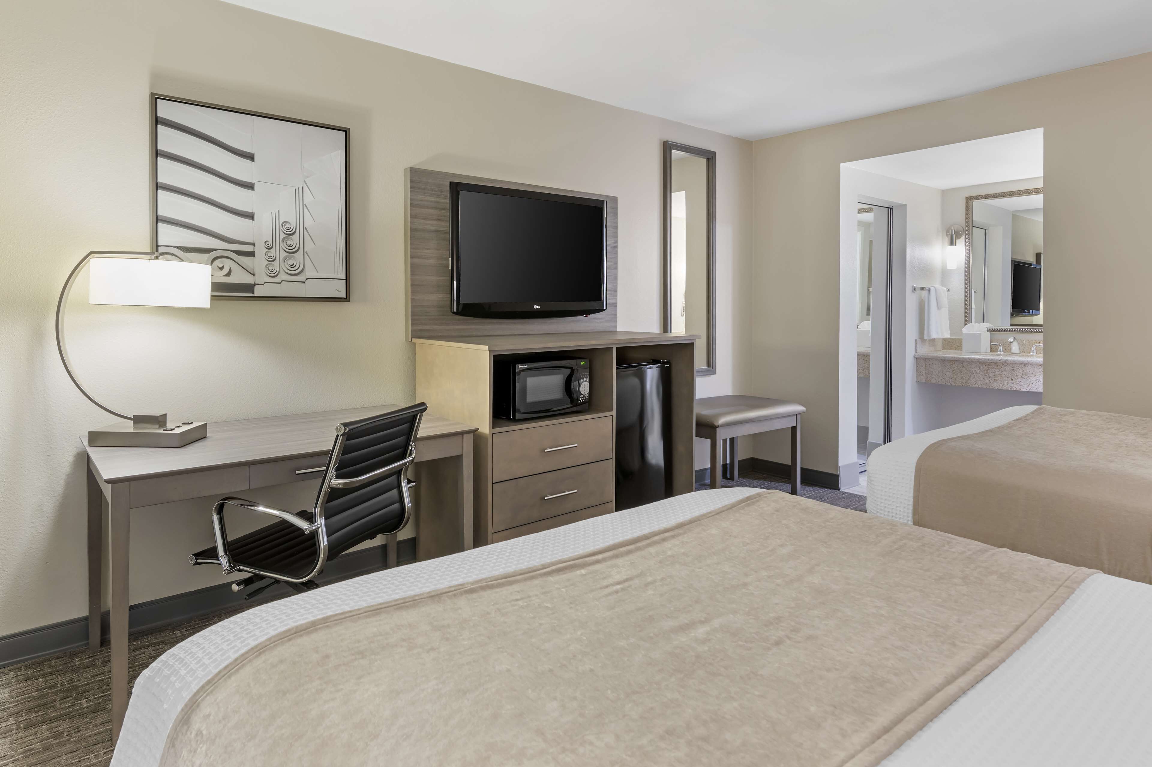 A hotel room with a bed, a desk with a chair, a television, a microwave, and a small table.