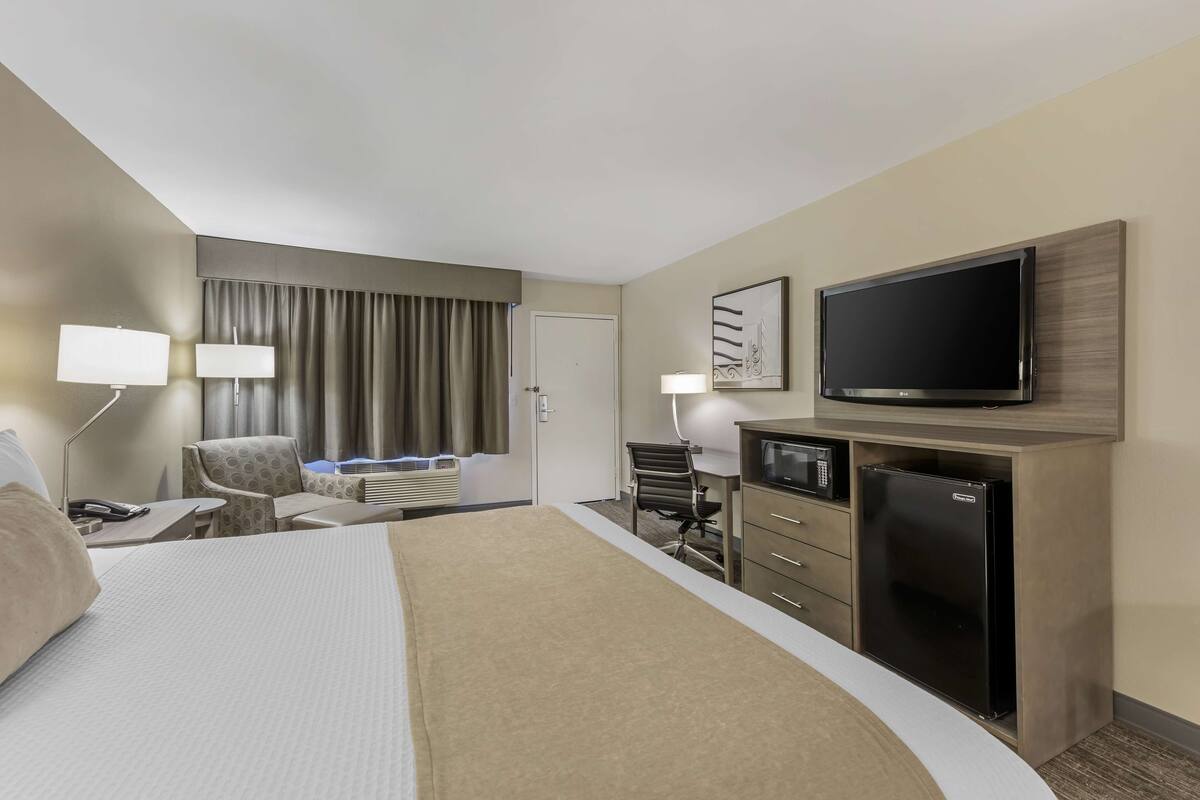 A hotel room with a bed, a desk with a computer, a television, and a minibar.