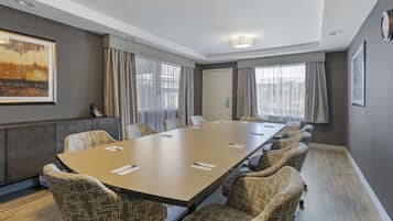 A conference room with a long table, patterned chairs, and large windows with curtains.