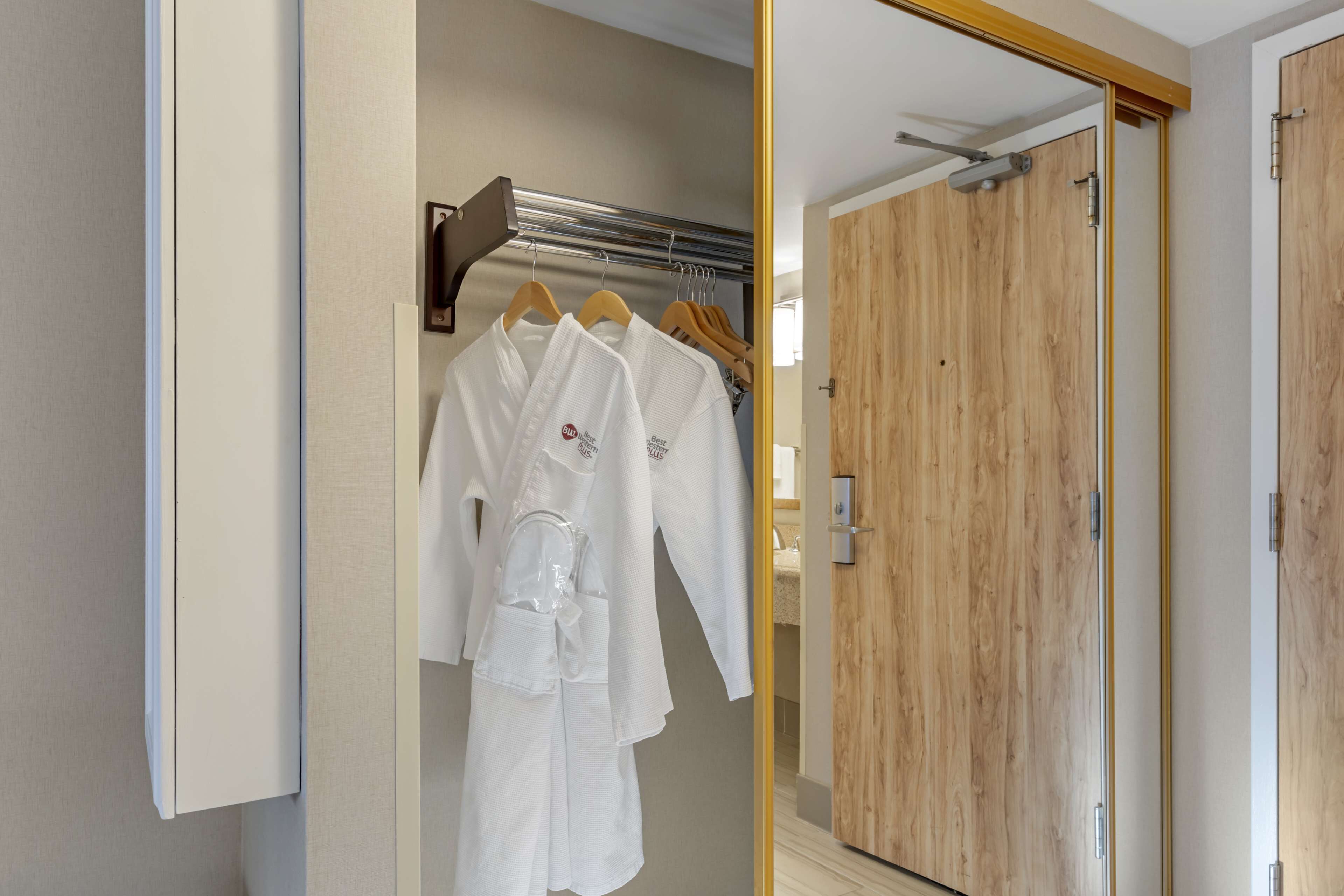 A hotel room with a wooden wardrobe, a mirror, and a clothing rack with white robes.