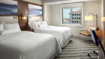 A hotel room with two beds, a desk, a chair, a lamp, and a window with a city view.