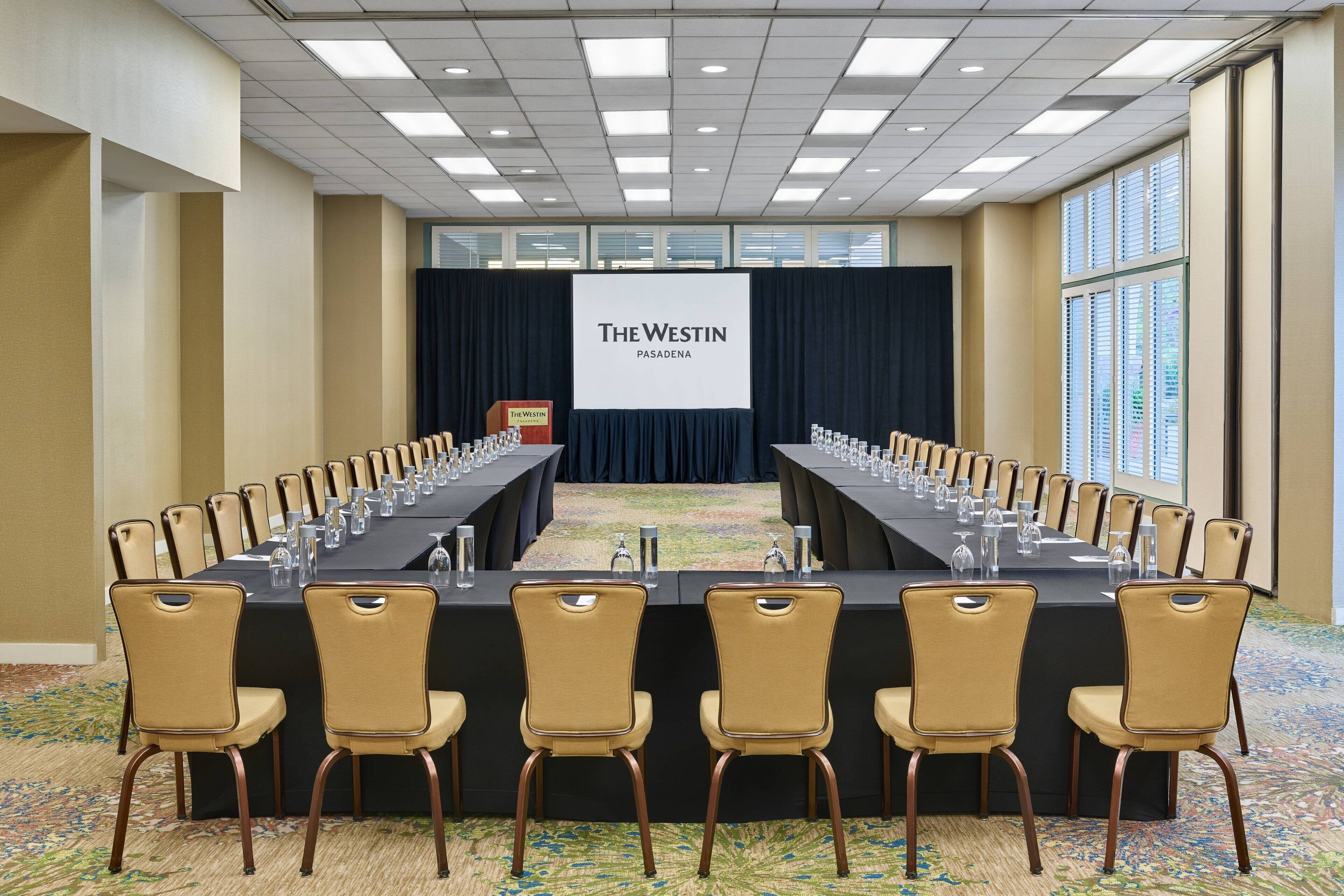 A conference room with a long table, chairs, and a screen displaying "The Westin Pasadena".