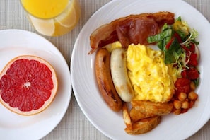 Un plato de desayuno con tocino, salchichas, huevos revueltos y una ensalada.