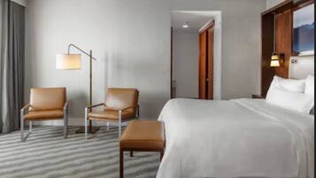 Habitación de hotel con cama, dos sillas, una lámpara de pie y vistas a las montañas a través de una ventana.