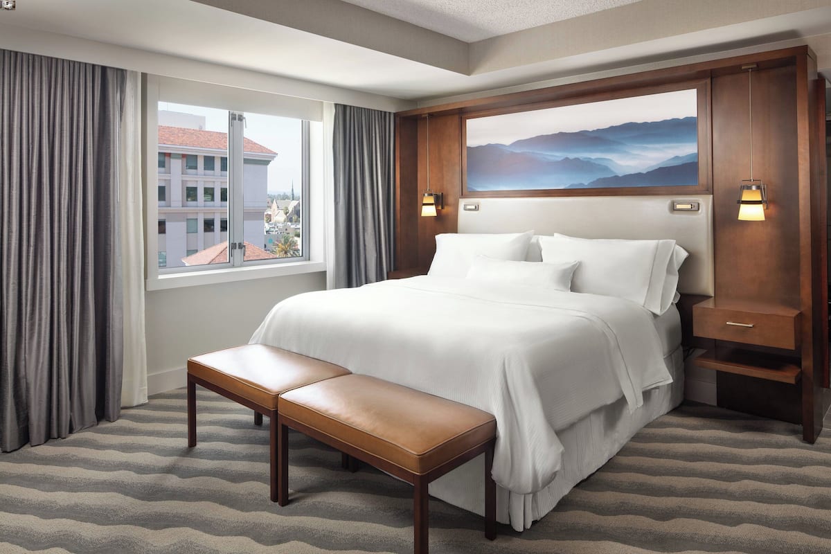 A hotel room with a large bed, a bench, a nightstand, and a painting on the wall.