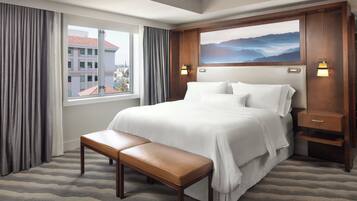 Habitación de hotel con una cama grande, un banco, una mesita de noche y un cuadro en la pared.