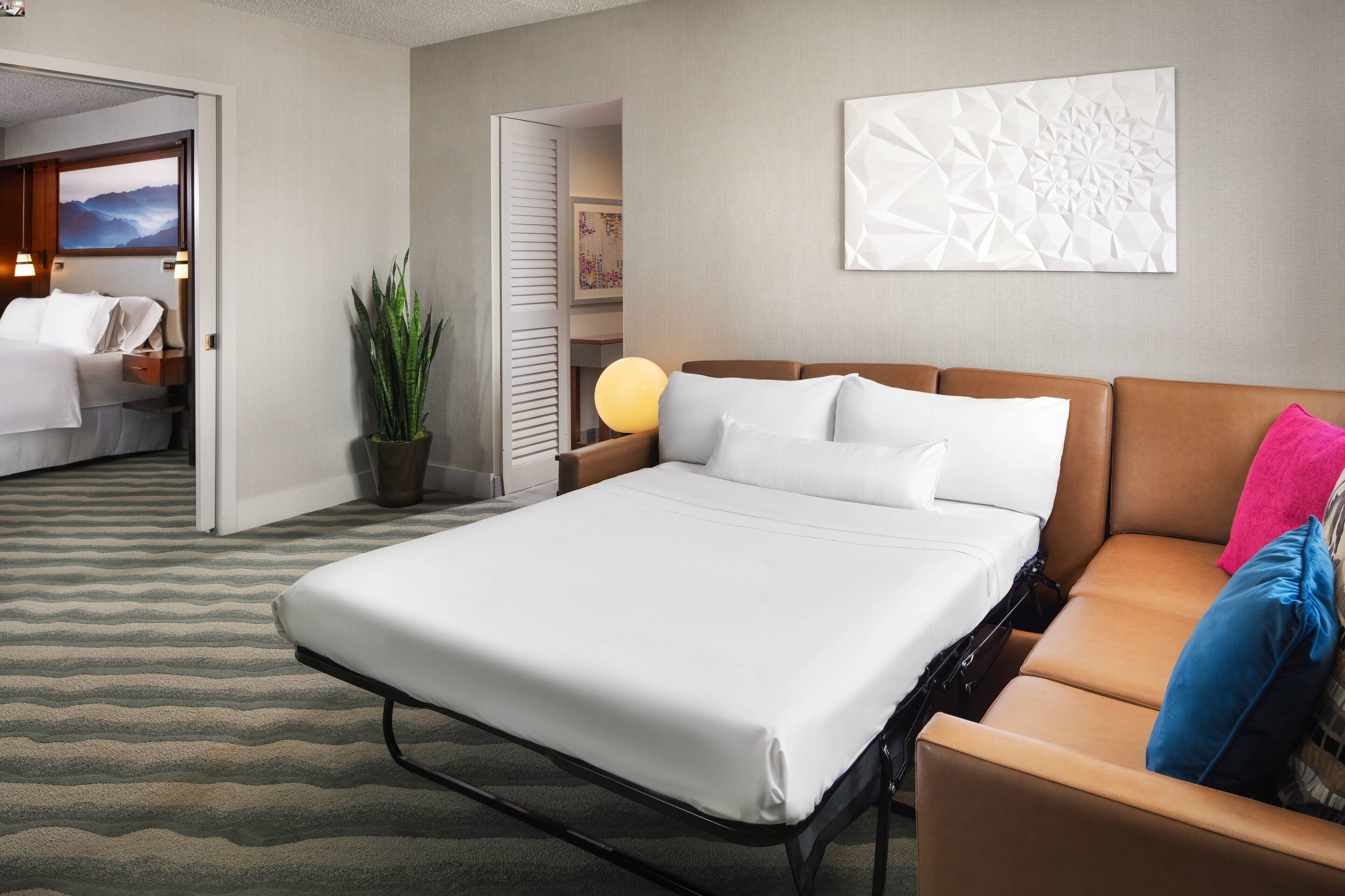 Habitación de hotel con cama, sofá, planta en maceta y lámpara fijada a la pared.