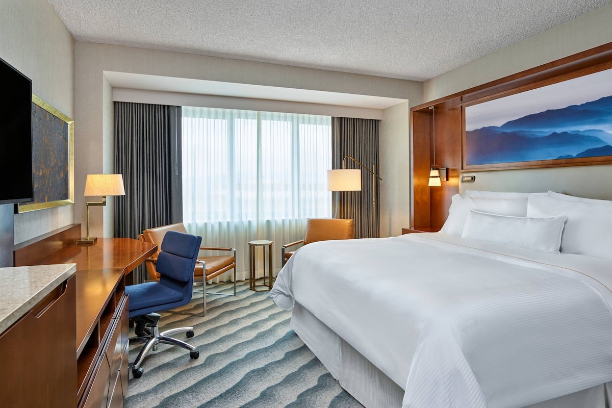 A hotel room with a large bed, a desk with a chair, a television, and a painting on the wall.