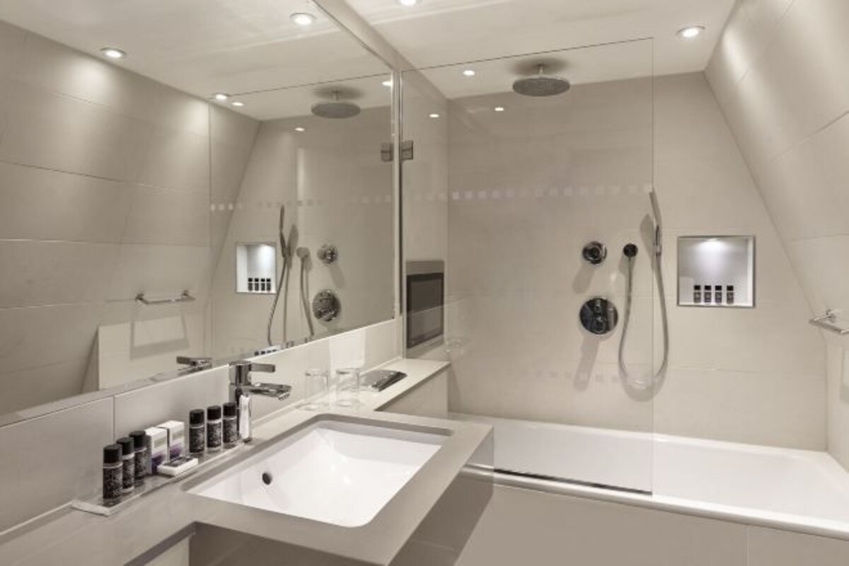 Une salle de bain moderne dotée d’un grand miroir, d’une baignoire, d’une zone de douche et d’un meuble-lavabo avec un évier et des articles de toilette.